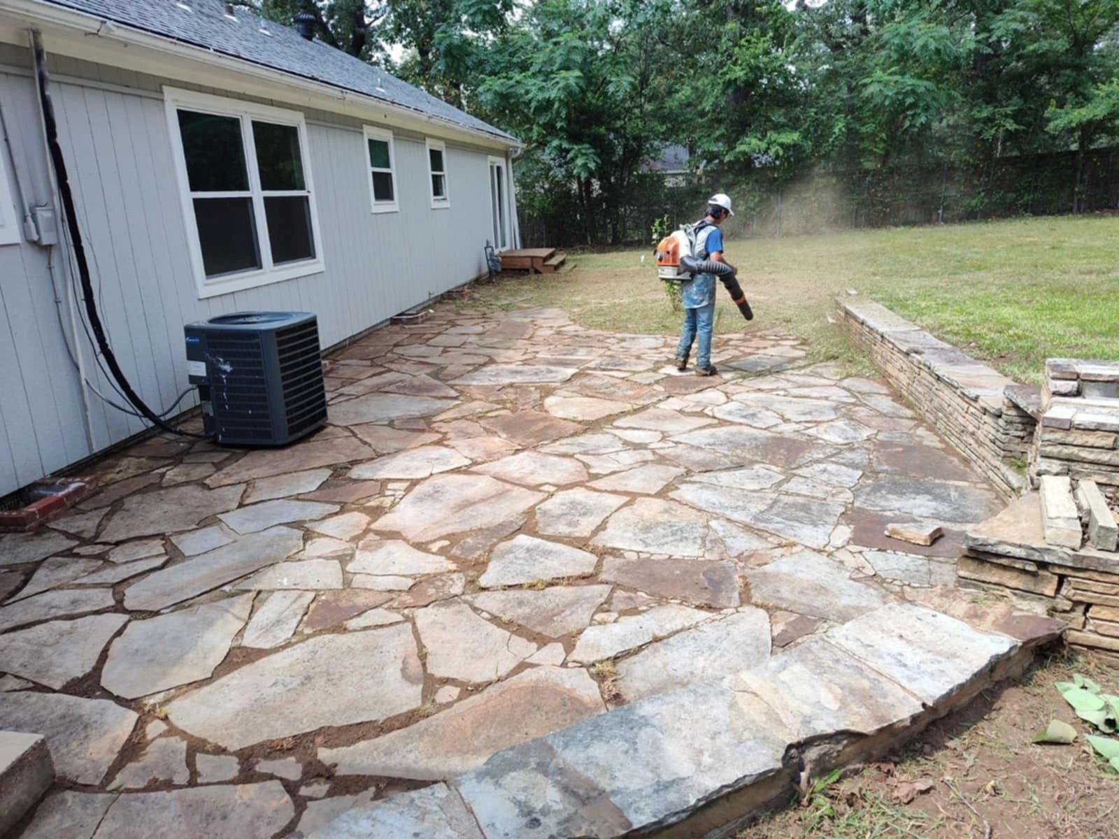Worker operating leaf blower on flagstone patio